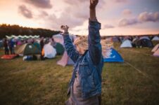 Festivalbesucherin hebt bei Sonnenuntergang die Arme zwischen Zelten