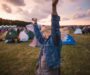 Festivalbesucherin hebt bei Sonnenuntergang die Arme zwischen Zelten