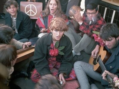 Hippiegruppe sitzt dicht beieinander mit Gitarre und Friedenssymbol