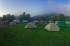 Viele Zelte und Menschen auf einer grünen Campingwiese im Morgennebel