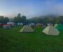Viele Zelte und Menschen auf einer grünen Campingwiese im Morgennebel